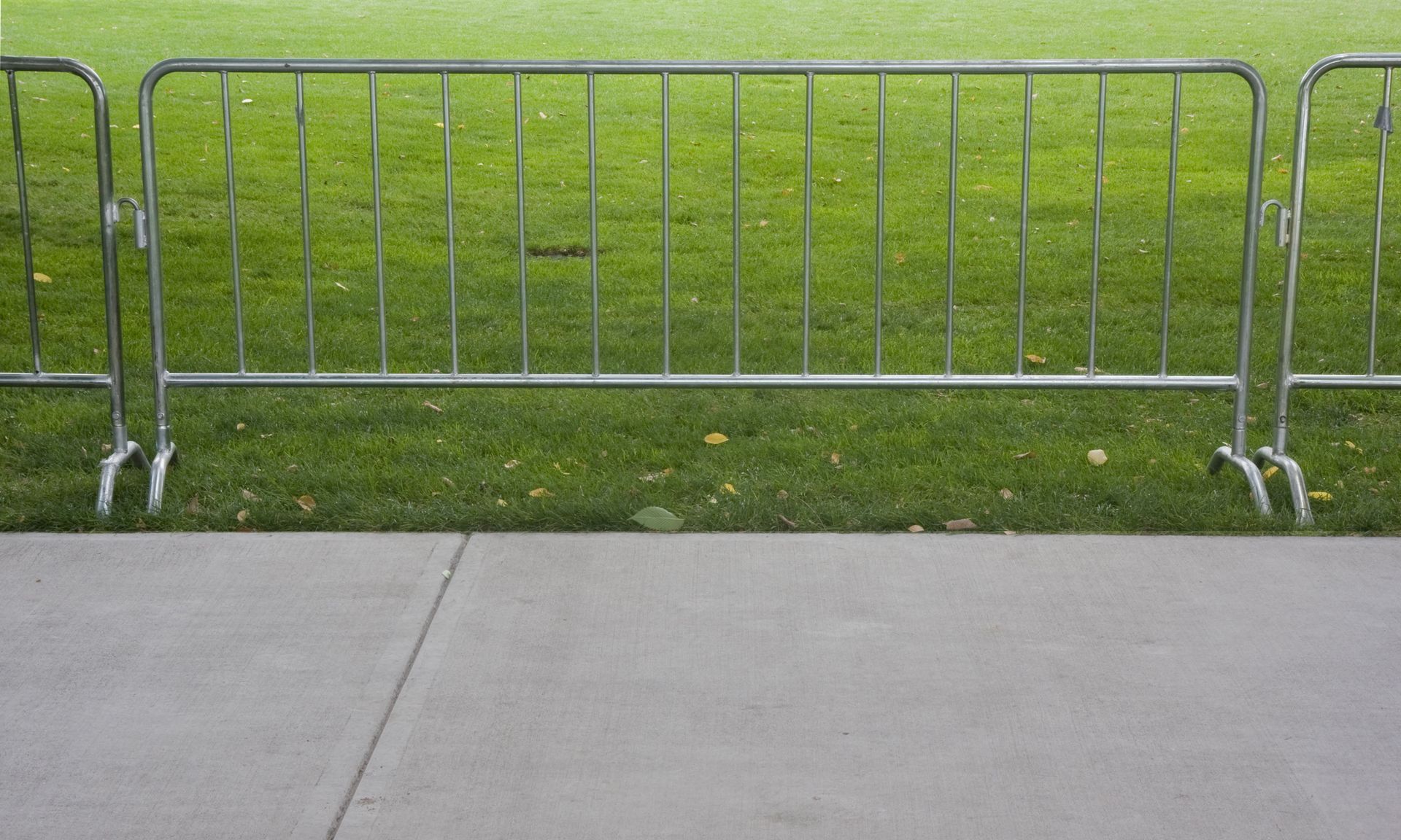 Metal crowd control barriers on a concrete sidewalk, with grass in the background.