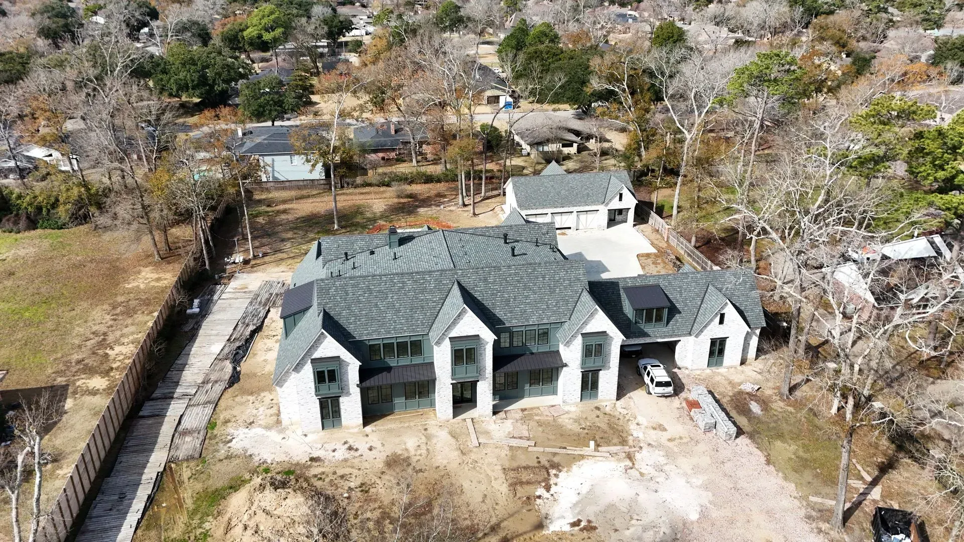 Aerial view of a large white house with a dark gray roof and attached garage, on a lot with bare trees.