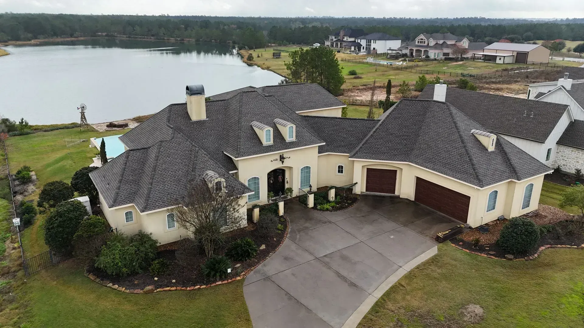 Luxurious beige house with gray roof, driveway, and lake view.