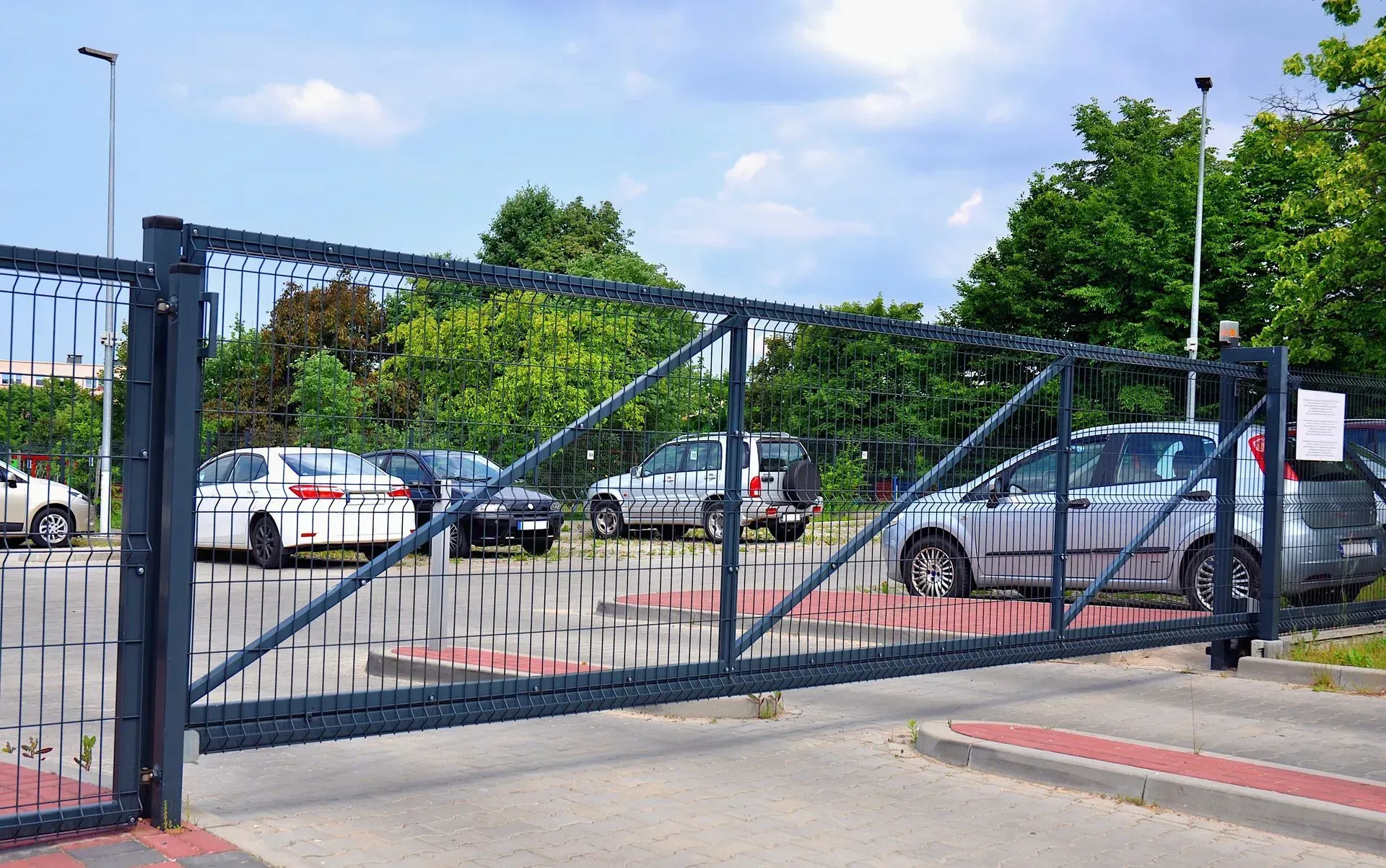 Closed, spiked metal gate at a parking lot entrance, with cars parked behind it on a sunny day.
