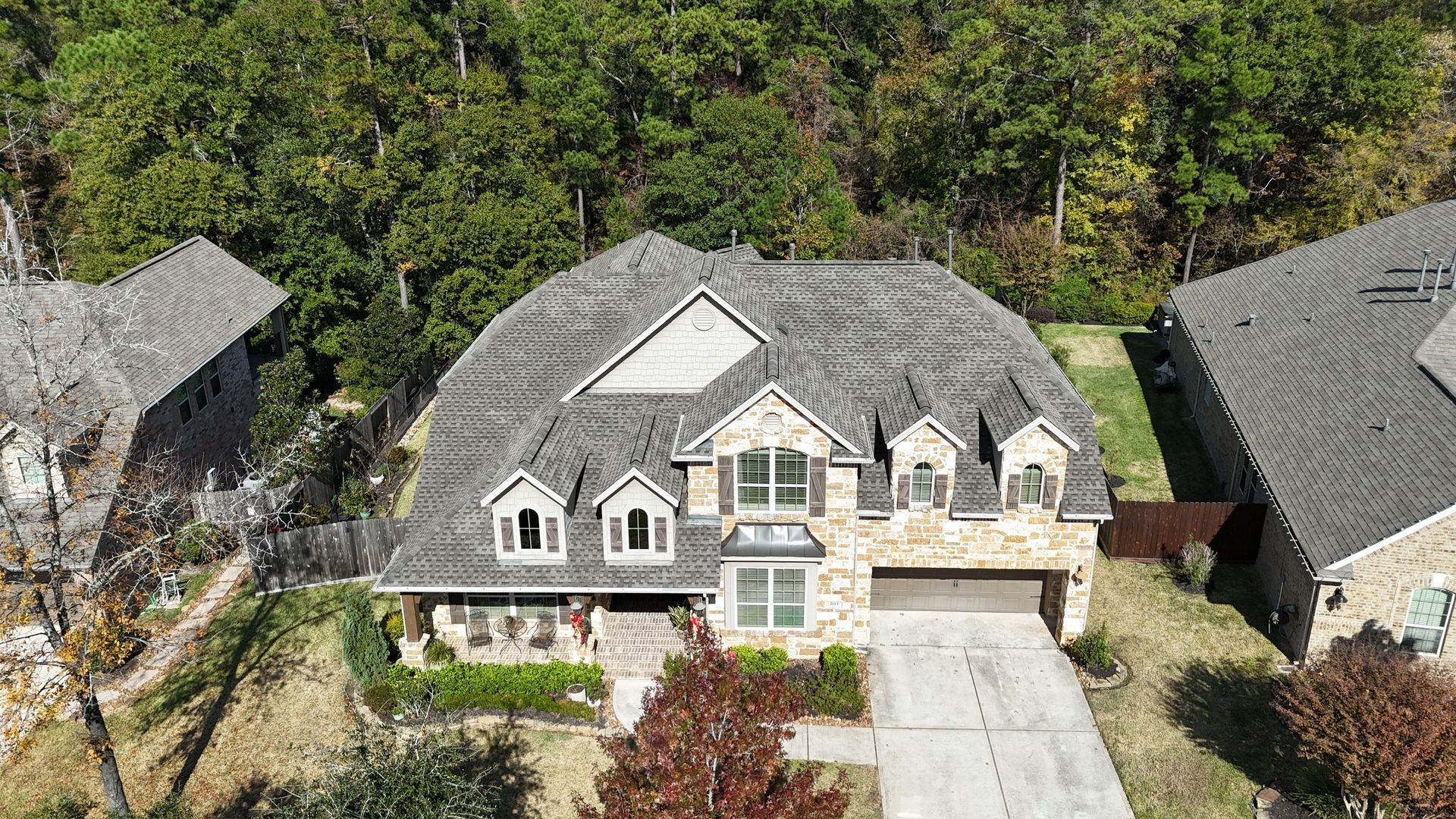 Overhead view of a two-story home with a stone and gray shingle exterior, surrounded by trees.