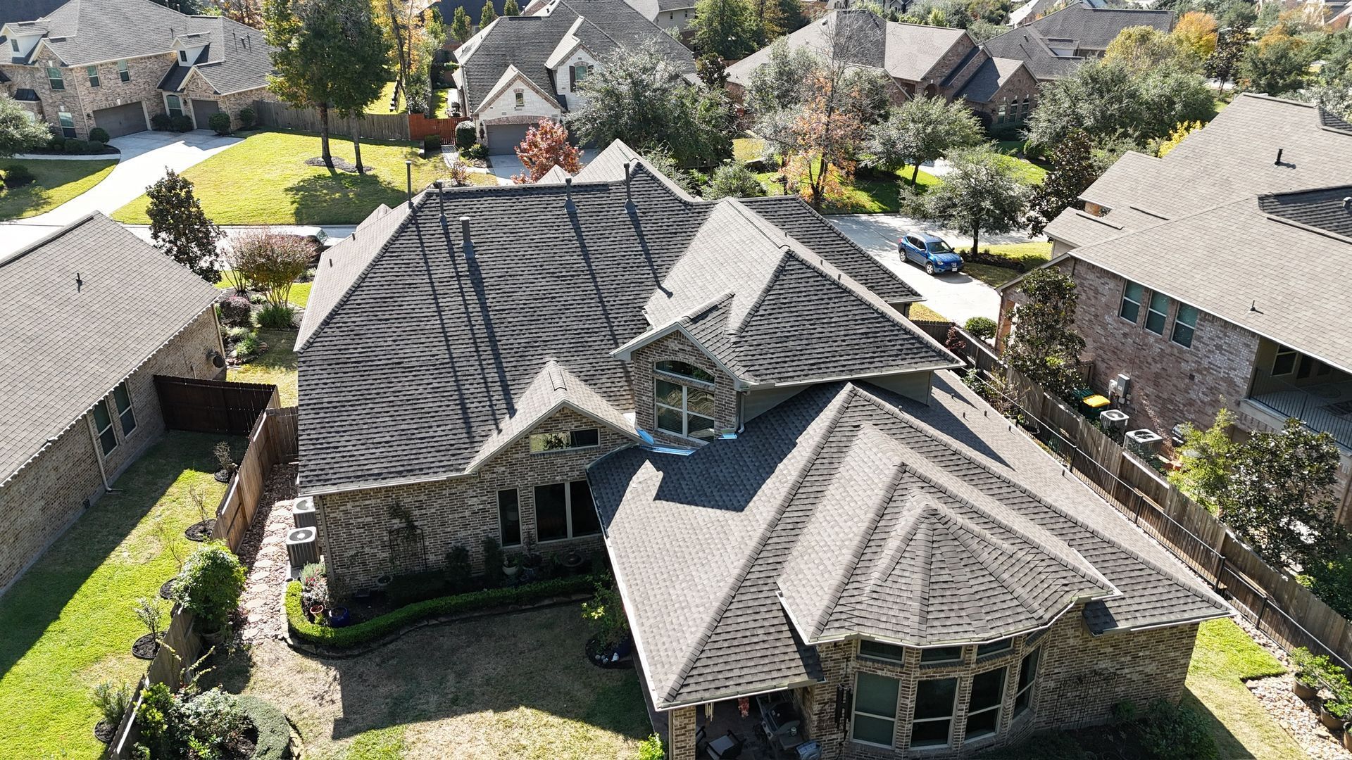 Aerial view of a large, brown-roofed house with surrounding green lawns and trees in a residential area.