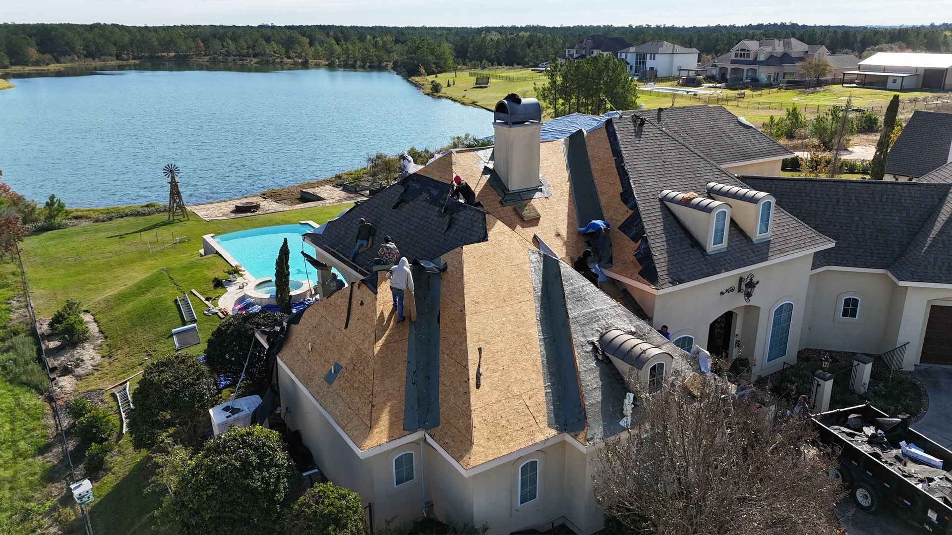 Roofers working on a house roof near a lake and pool.