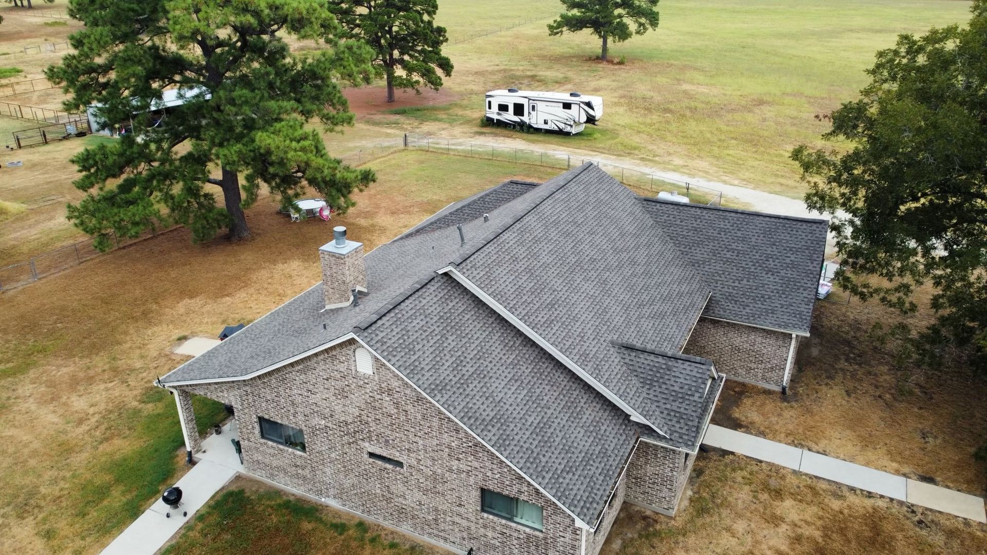 Overhead view of a house with a gray roof and rustic siding, with a recreational vehicle in the background.