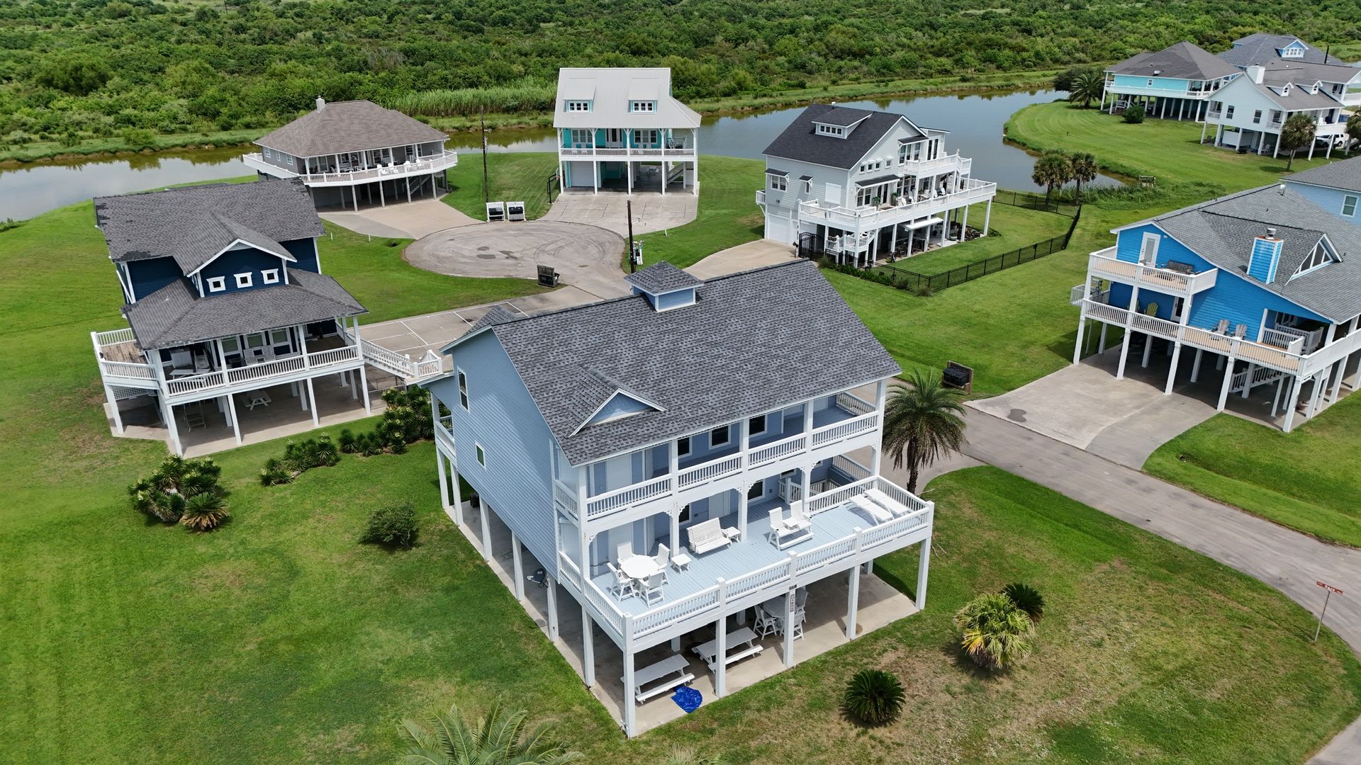 Aerial view of waterfront houses with elevated foundations and decks, on green lawns.