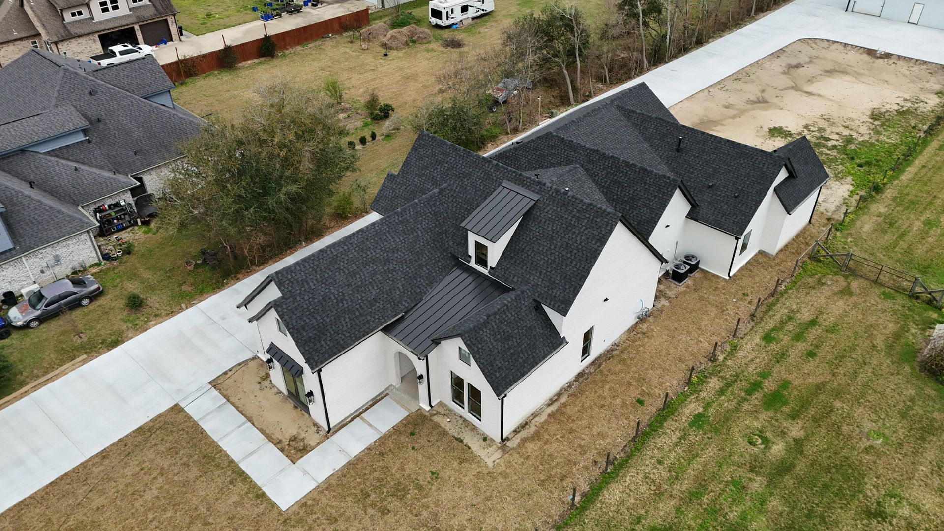 An aerial view of a white house with a dark roof and a long driveway surrounded by grassy land.