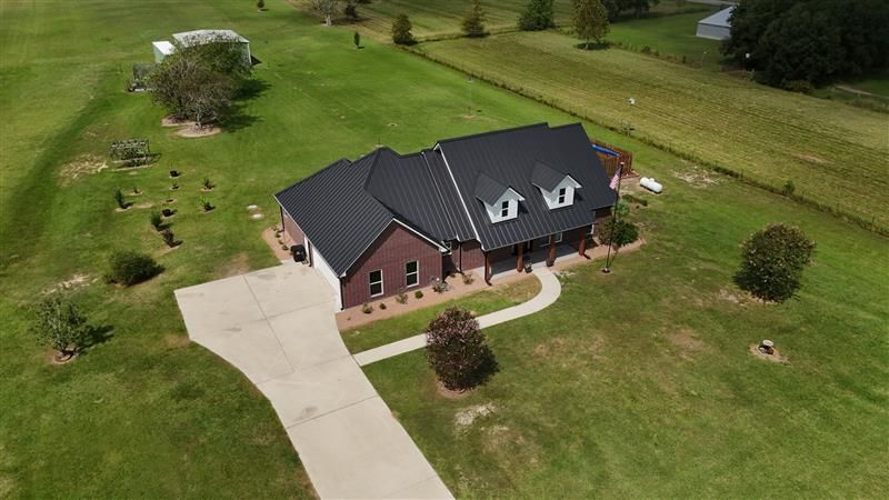 Brick house with a black roof and a long driveway on a large, grassy property.