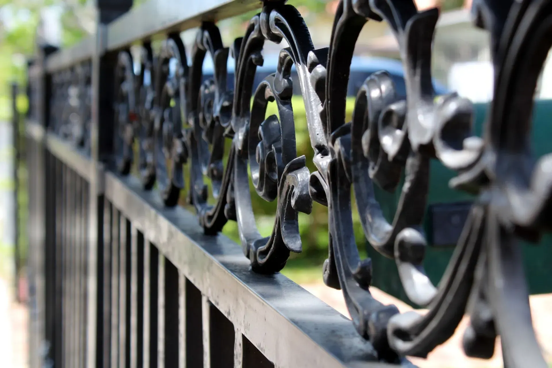 Black wrought iron fence, ornate scrolling design along top, with blurred background.