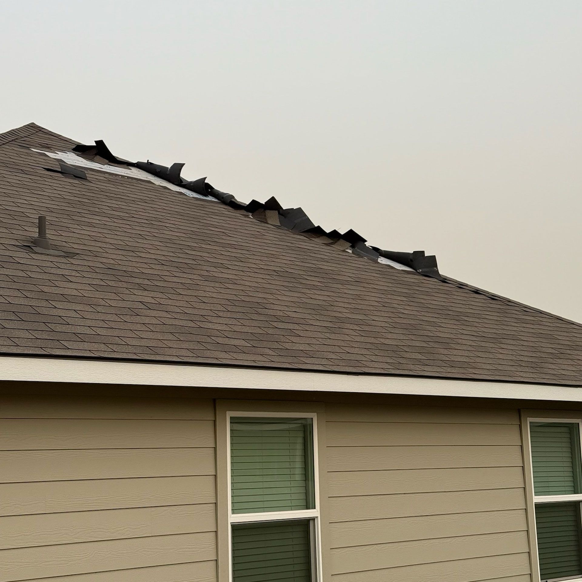 House with damaged roof and windows, cloudy sky.