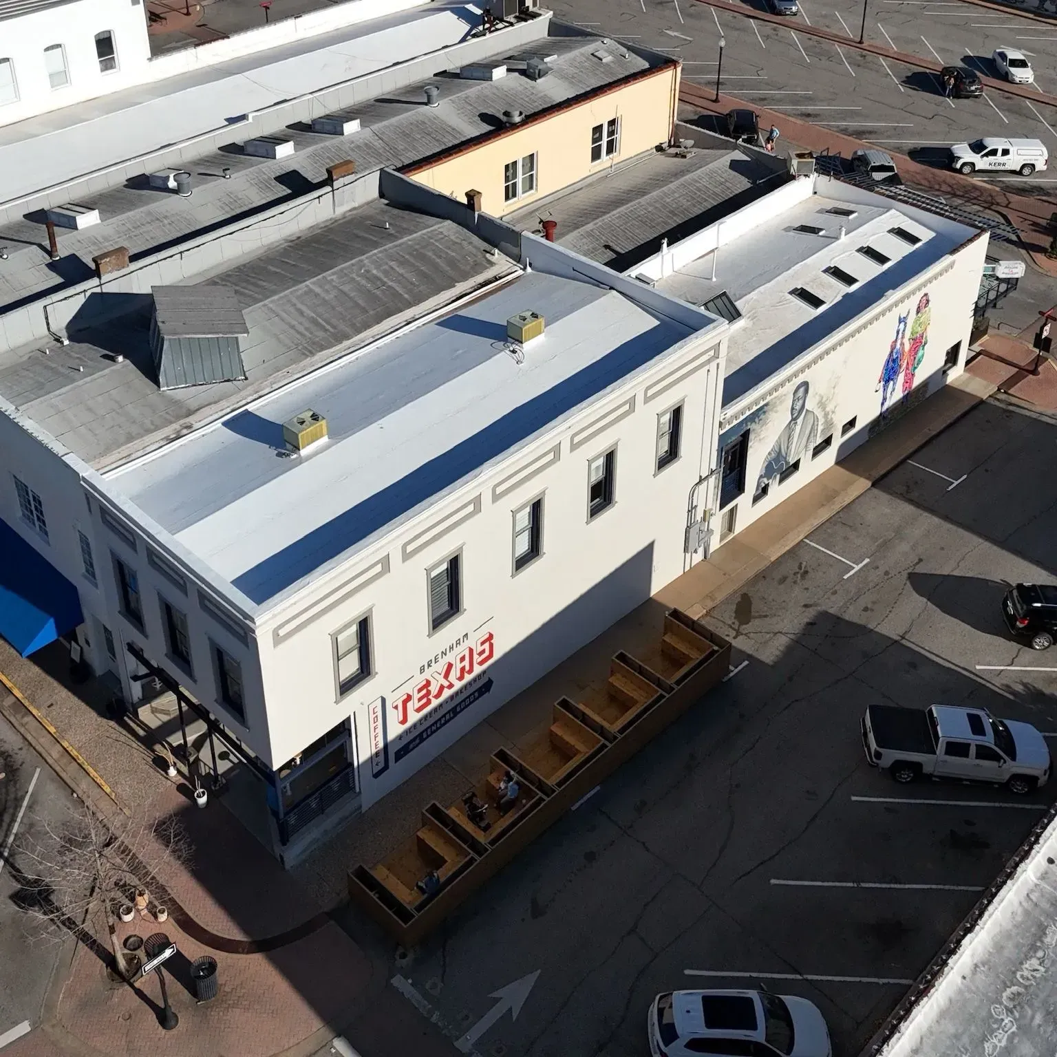 High-angle view of a downtown area with white buildings, storefronts, cars, and a mural.