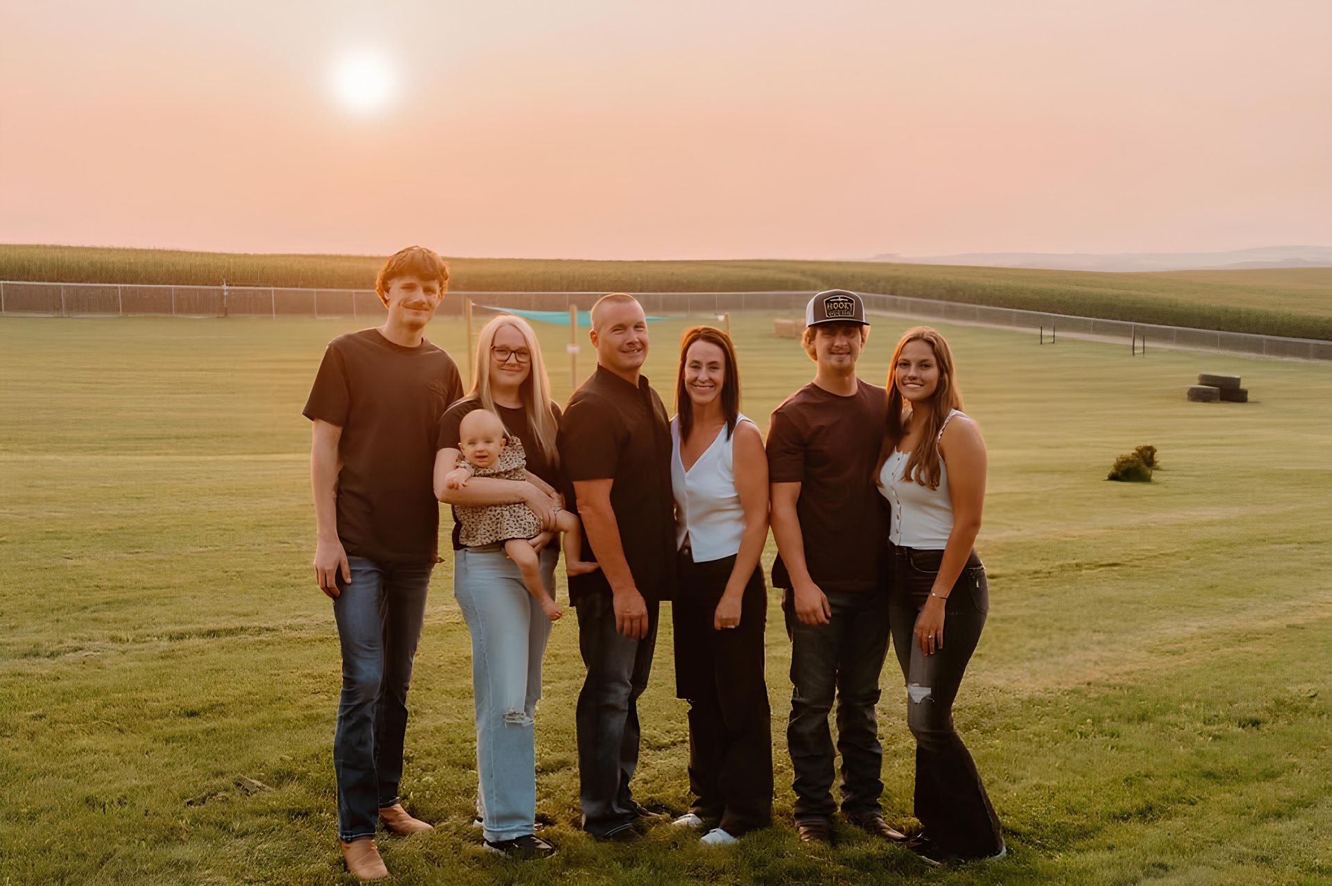 Family of seven posing on a grassy field at sunset.