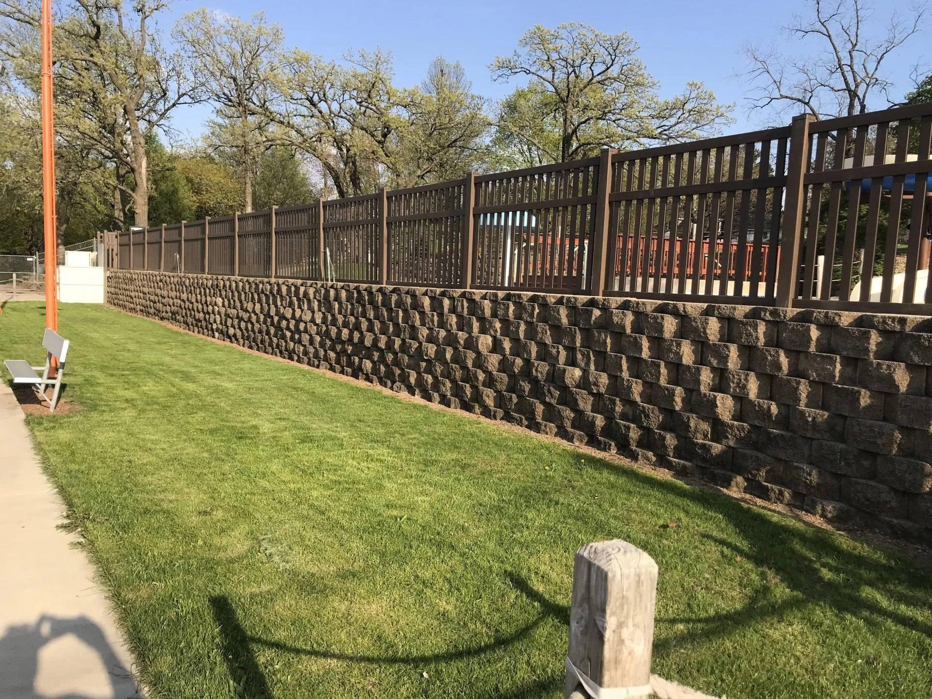 A retaining wall and brown fence along a grassy area under a blue sky.
