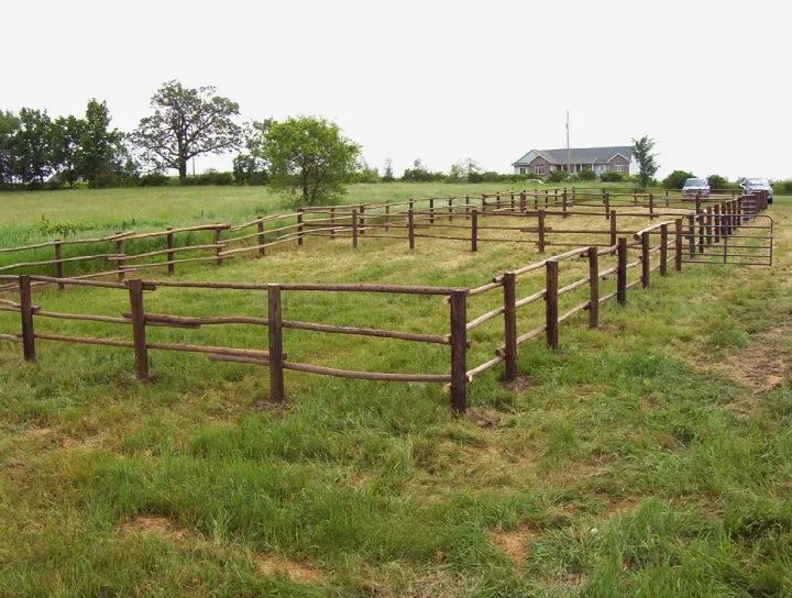 Wooden fence enclosure in a grassy field with a house in the background.