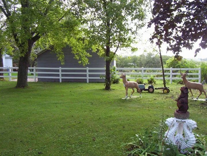 Green yard with white fence, trees, and lawn ornaments of deer and a bear.