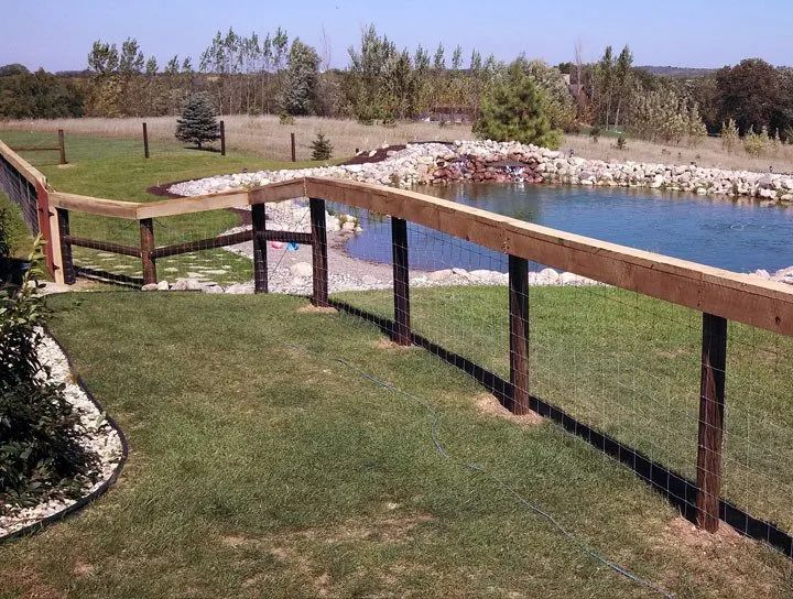 A wooden fence with wire mesh surrounds a pond in a grassy yard.