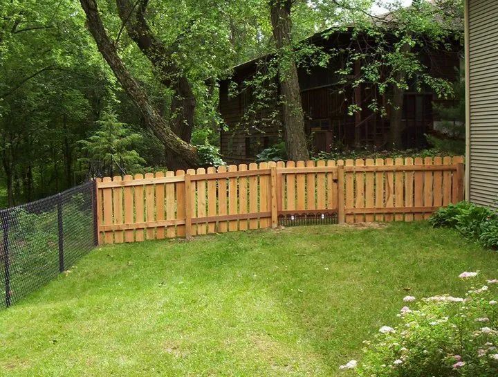 Wooden fence in a grassy yard, with a chain-link fence on the left and a building in the background.