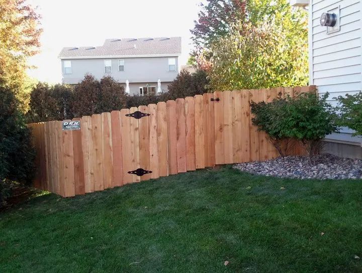 Wooden fence in backyard, built on a slope, with gate and landscaping.