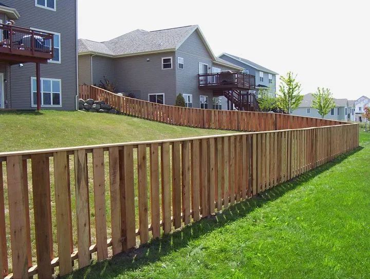 Wooden fence bordering the edge of a grassy backyard, adjacent to several houses.