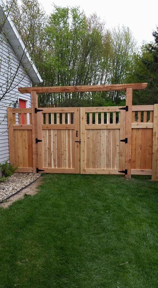 Wooden double gate with decorative top and side panels, leading into a grassy yard.