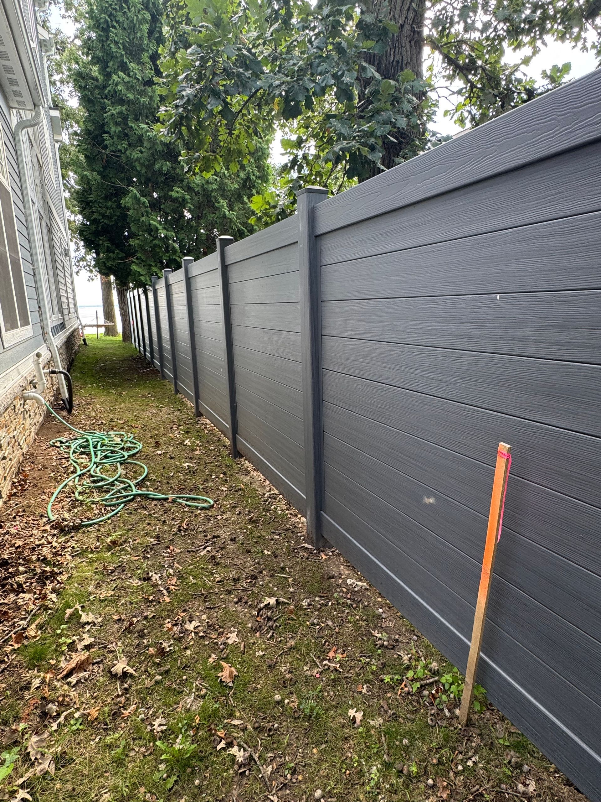 Dark gray horizontal slat fence next to grass and a building.