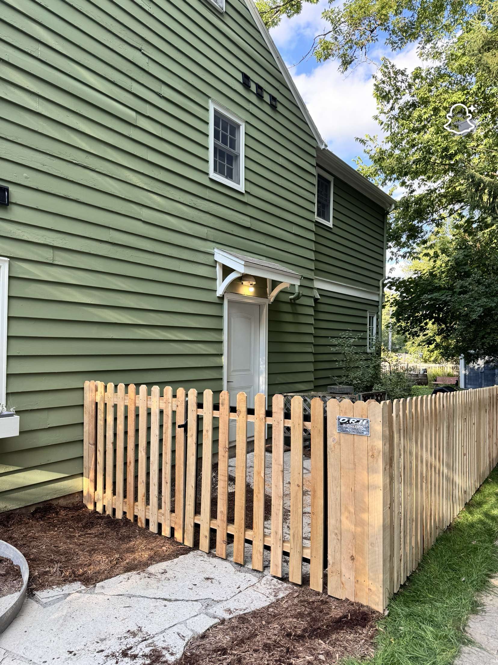 Green building with wooden picket fence and a covered entrance.