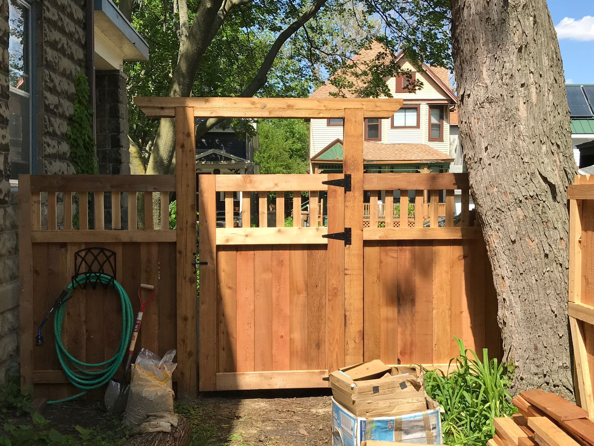 Wooden gate in a backyard, with a hose holder on the left.