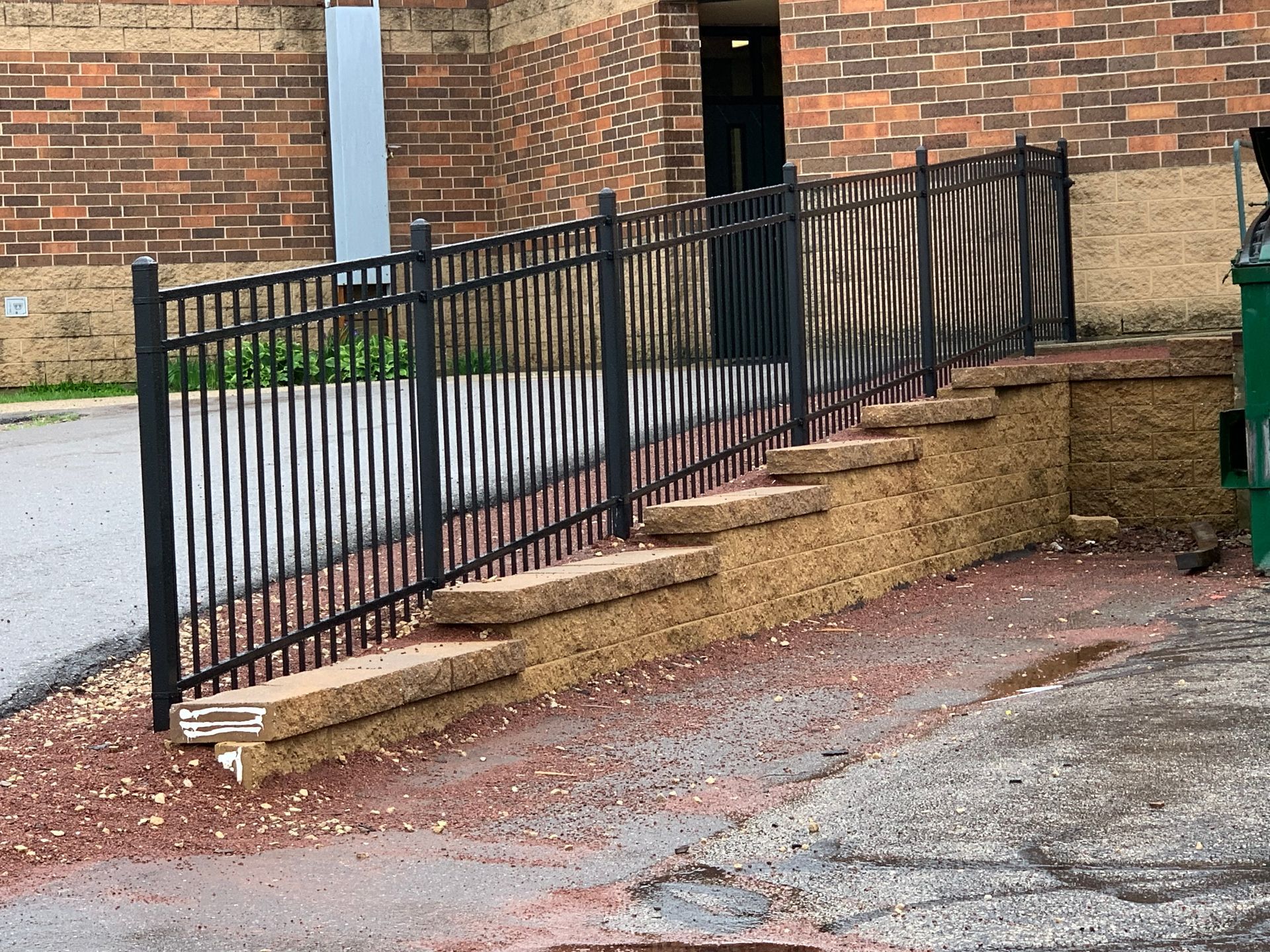Black metal fence with ramp and steps next to brick building.
