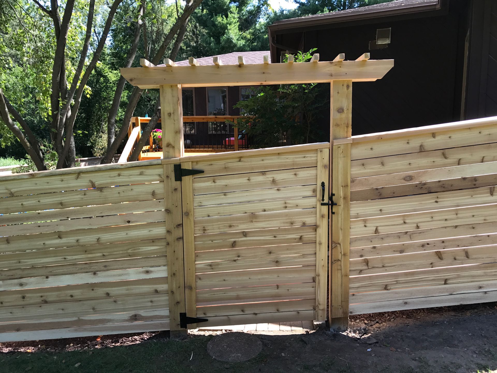 Wooden gate with pergola archway in a horizontal slatted fence.