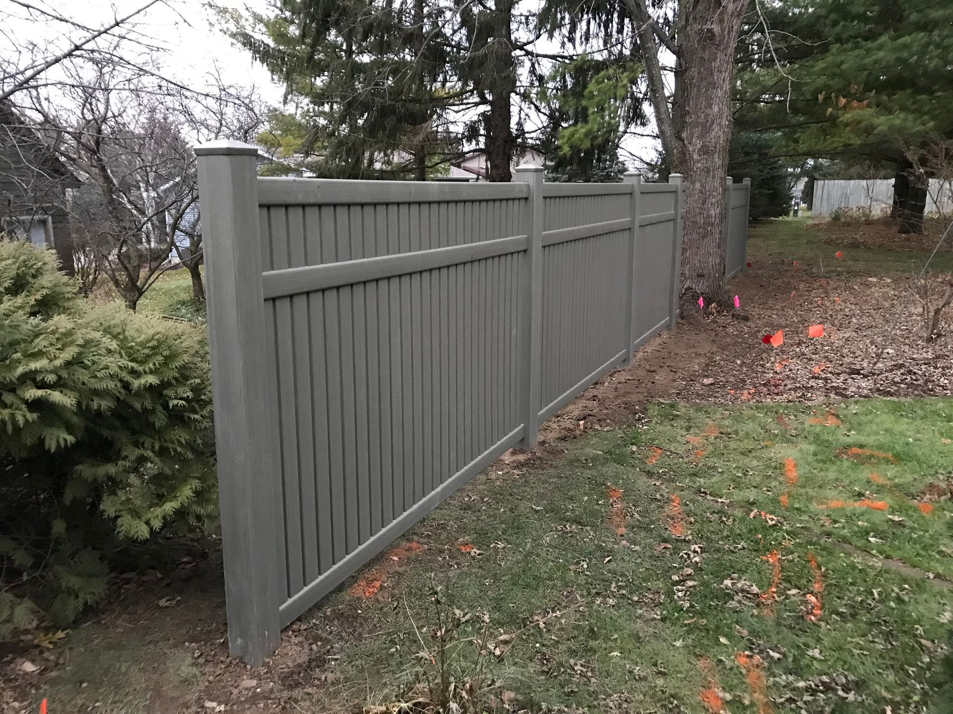 Gray vertical plank fence in a grassy yard, trees in the background.