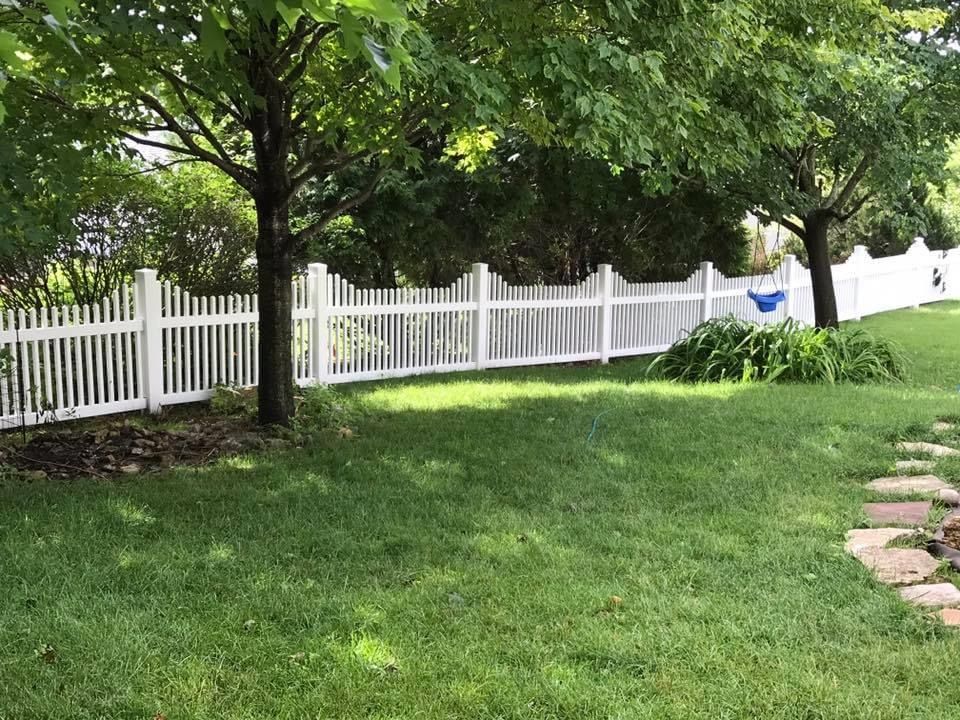 White picket fence in a grassy yard, with trees providing shade.