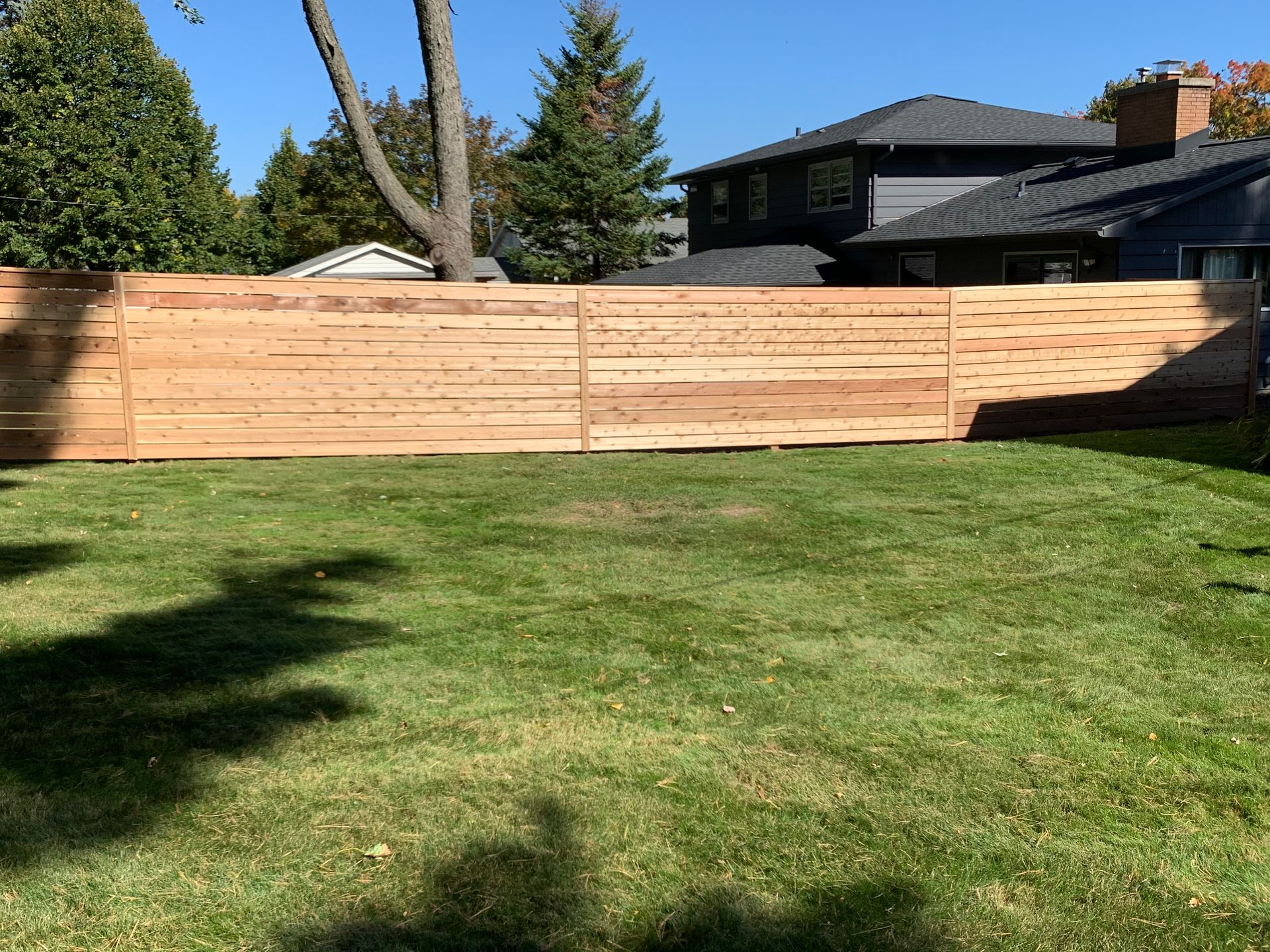A newly built wooden fence in a grassy backyard, with a house visible in the background.