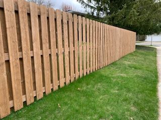 Wooden fence bordering green grass next to a sidewalk.