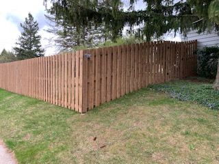 Wooden fence around a grassy yard, cornering at right angles. Trees in the background.