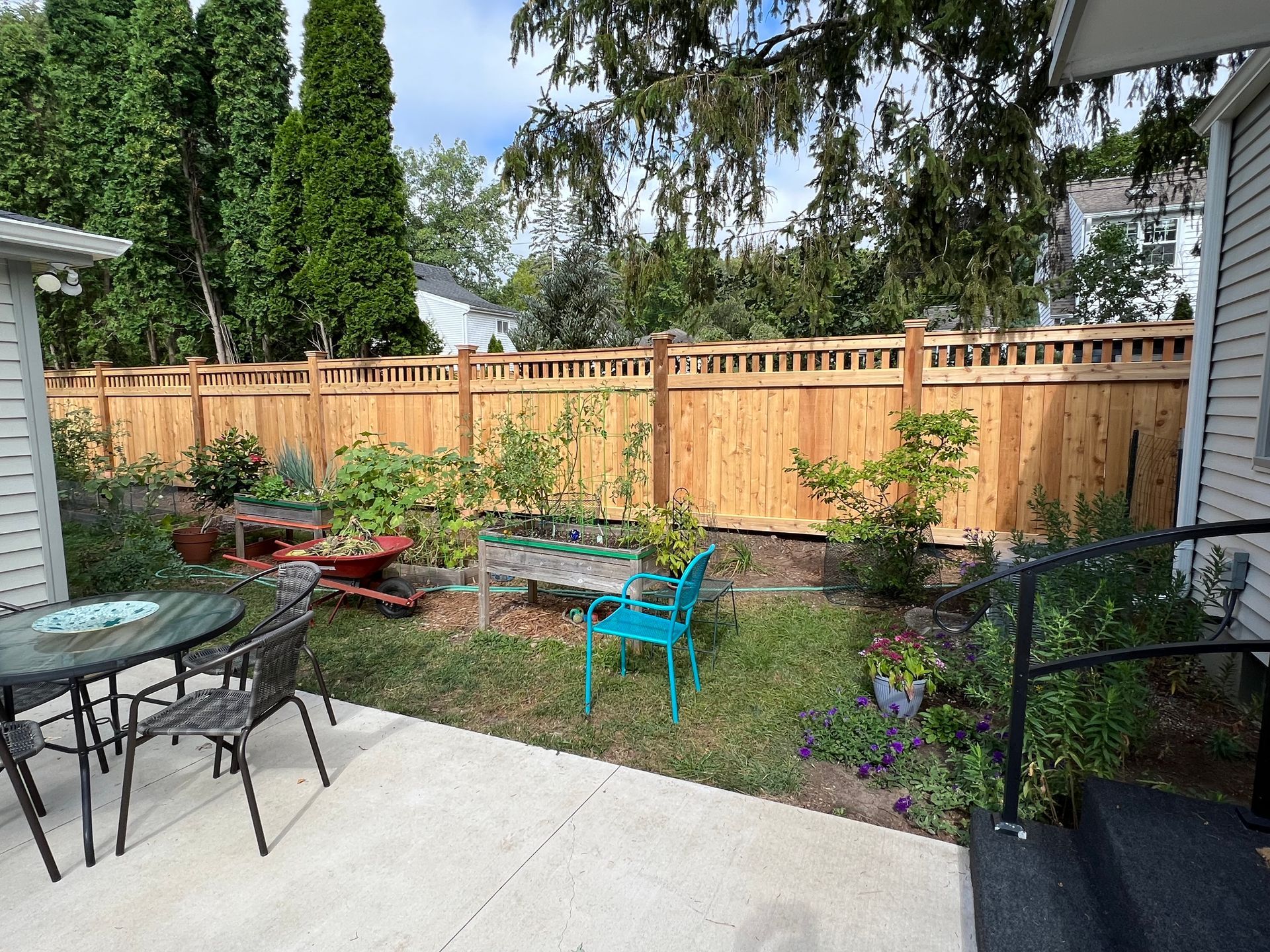 Backyard with a wooden fence, patio furniture, garden beds, and greenery.