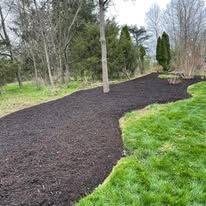 Freshly mulched garden bed beside a green lawn with trees in the background