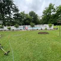 Backyard lawn with a white above-ground pool, trees, and a garden hose in the foreground.