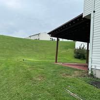 Grassy hill beside a white house with a covered porch and overcast sky