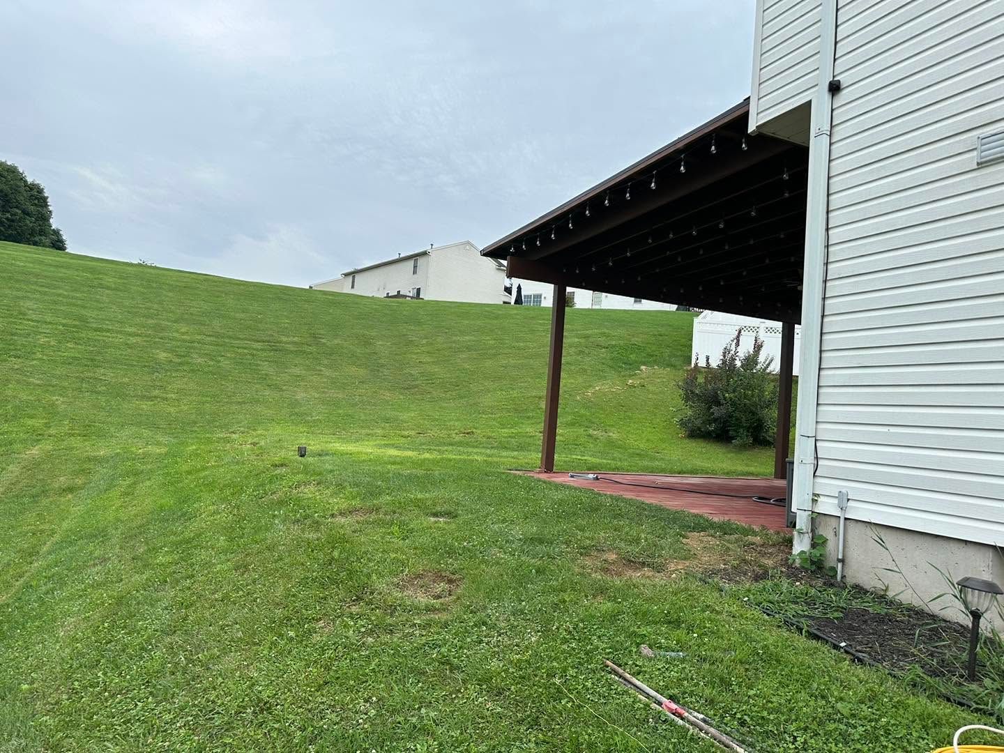 Grassy backyard beside white house with covered porch and cloudy sky
