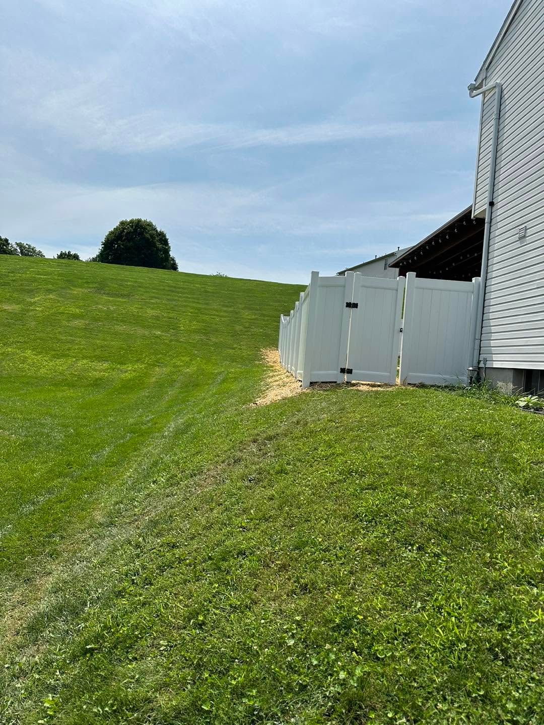 Grassy hill beside a white barn and fence under a partly cloudy sky