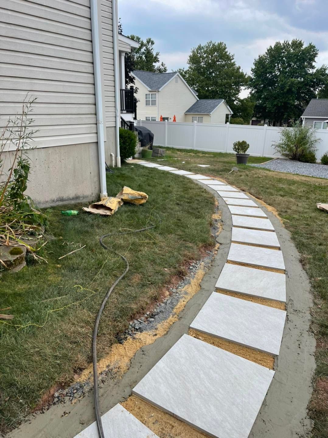 Curved walkway with white stepping stones set in fresh concrete beside a house and grassy yard