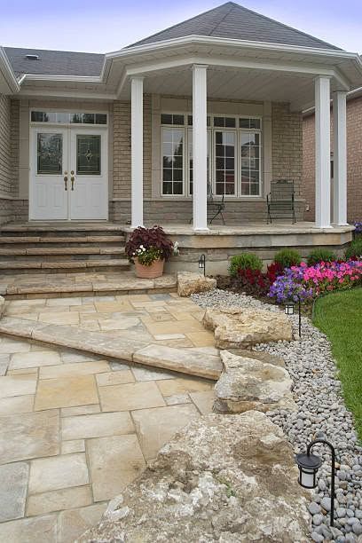 Front porch with stone steps, white columns, and a landscaped walkway leading to a brick house.