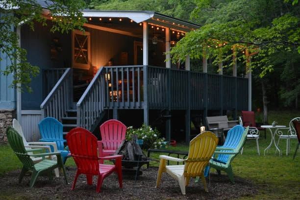 Colorful Adirondack chairs around a fire pit outside a lit cabin at dusk