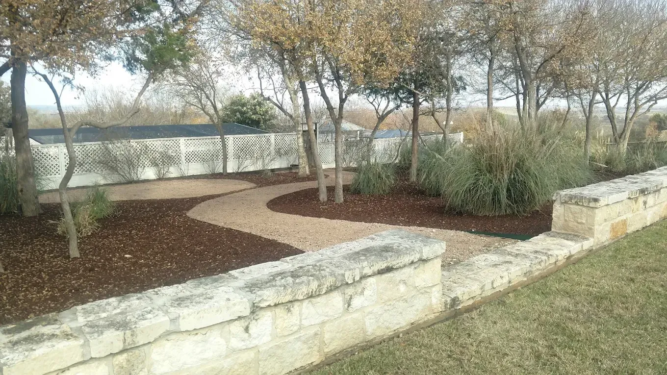 Stone pathway curves through a garden with trees and shrubs, bordered by a stone wall.