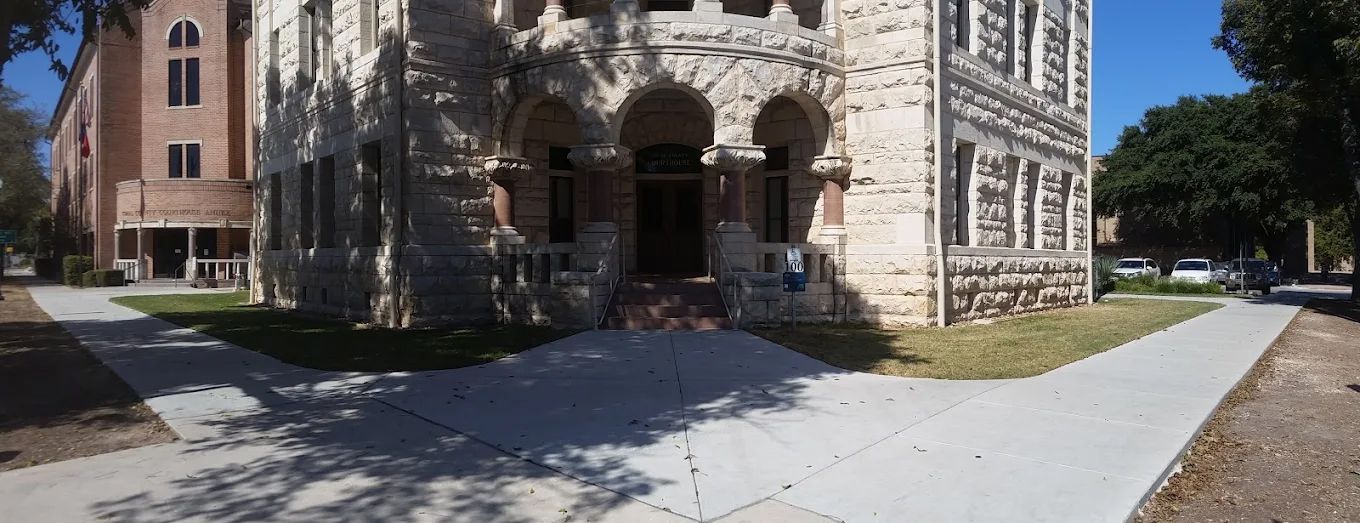 Stone building with arched entrance and sidewalk on a sunny day.