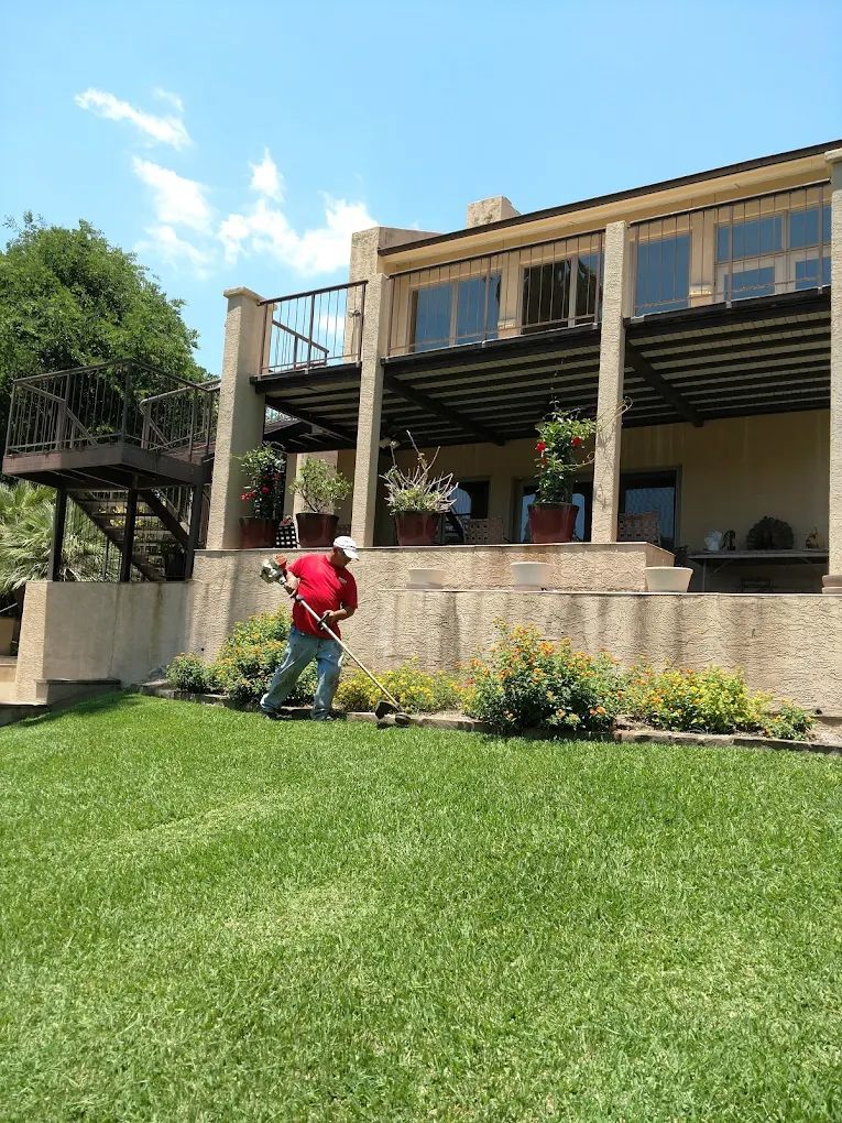 Man using weed trimmer on a green lawn in front of a multi-story building with a balcony.