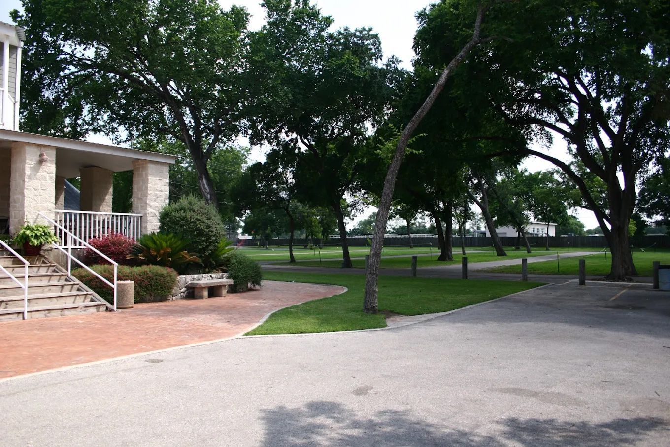 Building with stairs, brick patio, and green lawn leading to a park with trees.