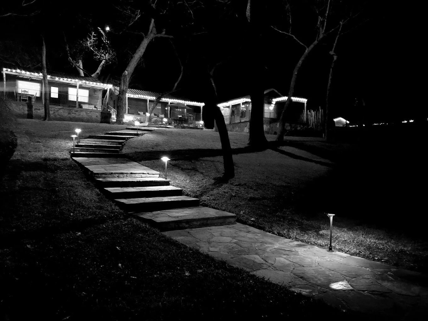Stone steps and pathway lead toward a house illuminated by lights at night.