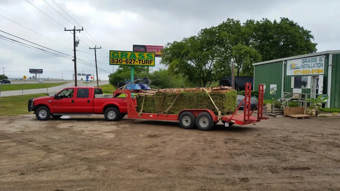 Red truck towing a trailer loaded with greenery at a roadside market on a cloudy day.