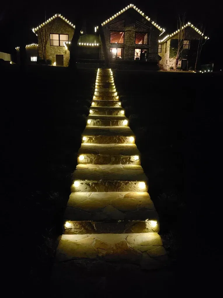 Lit steps lead to a house at night, framed by string lights and illuminated windows.