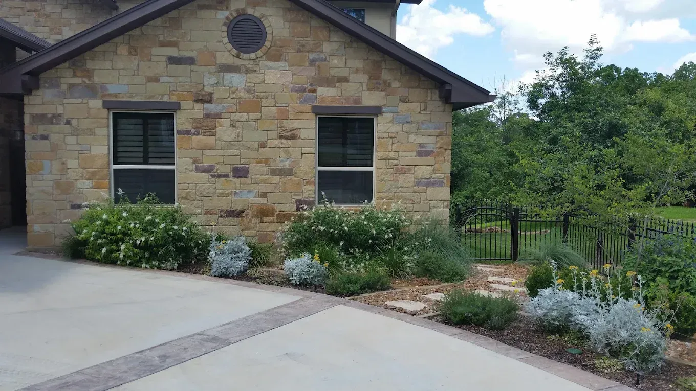 Stone house exterior with driveway and landscaped flower beds.